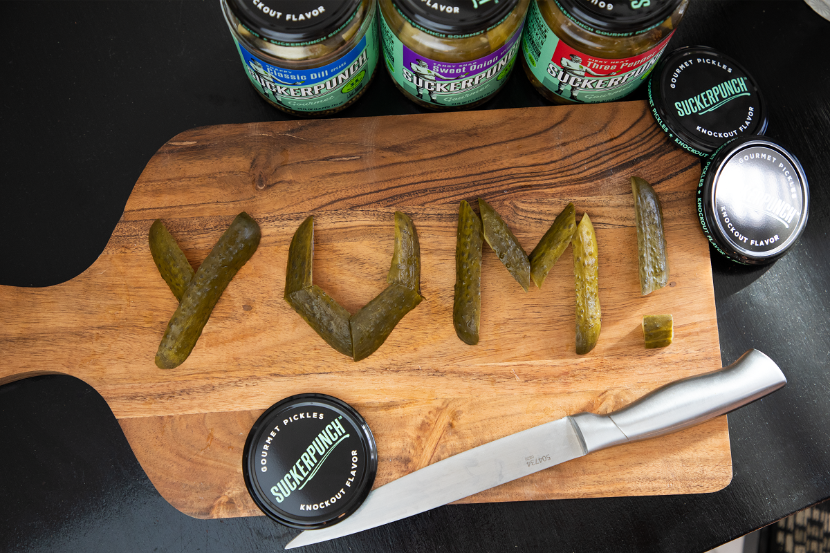Cutting board with word "Yum!" spelled with pickles